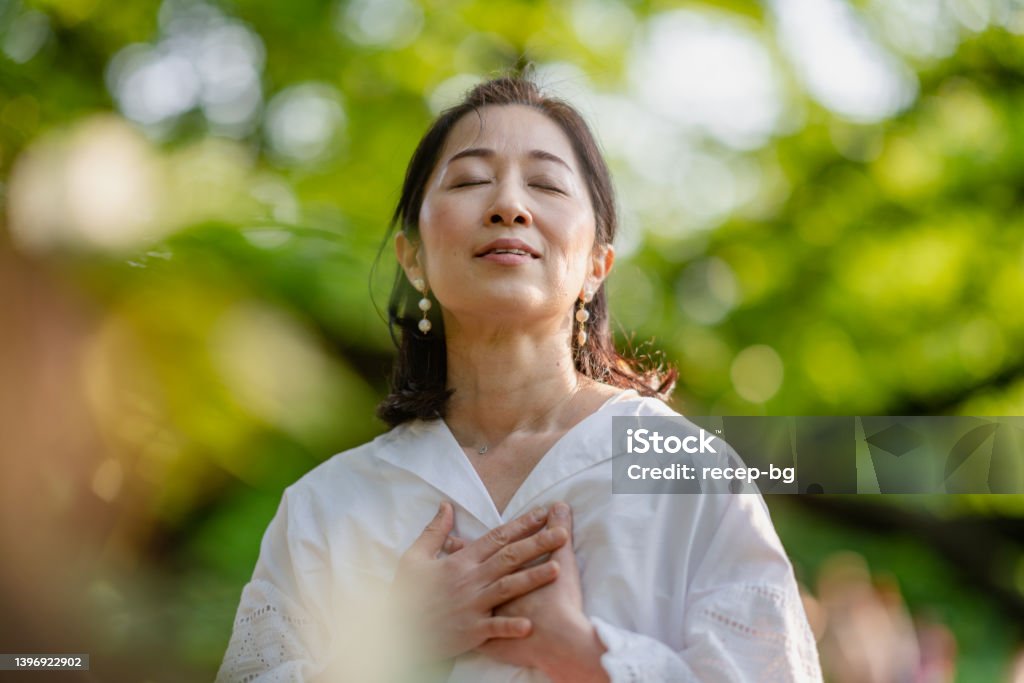 Woman meditating in nature A woman is closing her eyes, doing breathing exercise and meditating in nature. Women Stock Photo