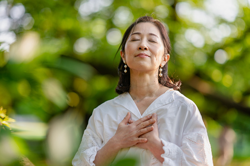A woman is closing her eyes, doing breathing exercise and meditating in nature.