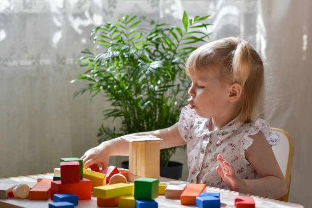 istock One two-year-old girl is sitting at a table and assembling a wooden construction kit. A child constructs a tower of cubes. 1396924112