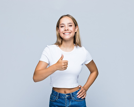 Portrait of smiling teenage girl gesturing thumbs up while standing against white background.