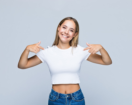 Portrait of smiling teenage girl pointing fingers at t-shirt against white background.