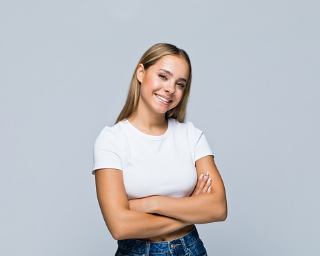 Portrait of smiling teenage girl with arms crossed standing against white background.
