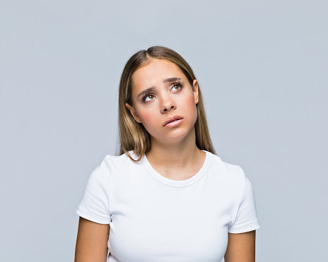 Contemplative teenage girl in t-shirt looking up against white background.