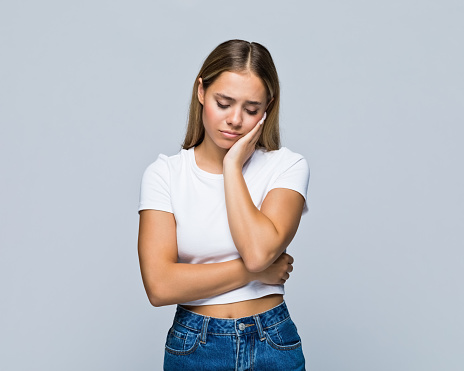 Depressed teenage girl with head in hand standing against white background.