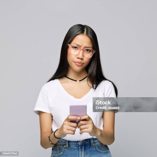 Confused Woman With Smart Phone Against Gray Background Stock Photo - Download Image Now