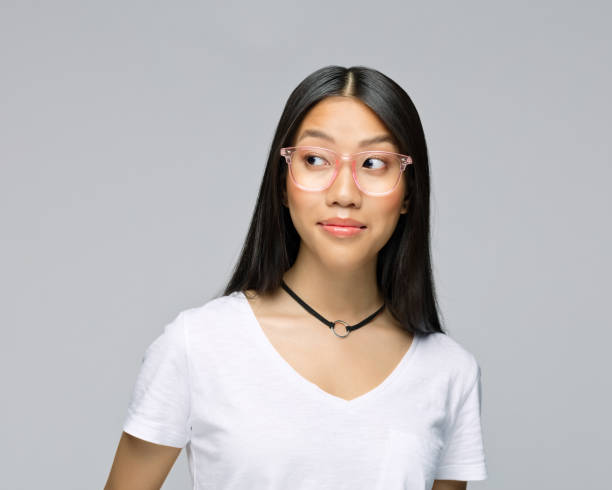 Curious woman against gray background Curious young woman in eyeglasses looking away while standing against gray background sideways glance stock pictures, royalty-free photos & images
