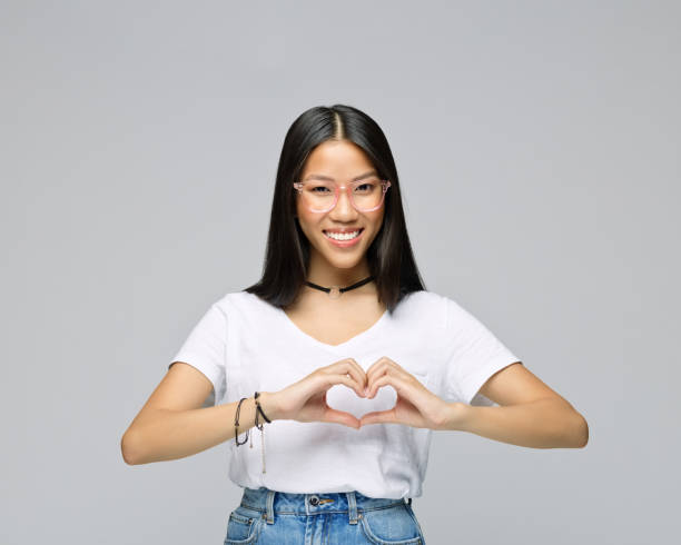 istock Woman gesturing heart shape against gray background 1396929672