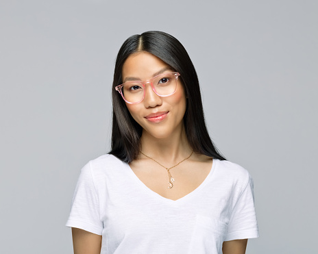 Portrait of smiling woman wearing eyeglasses standing against gray background
