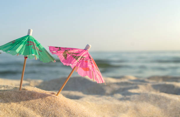 istock Three small paper cocktail umbrellas stand in sand on sandy beach close-up. 1396931702