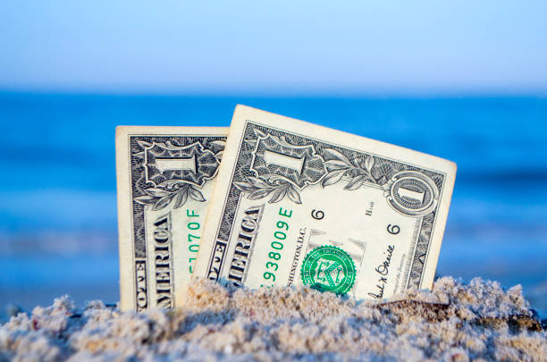 istock Two one dollar bills half buried in sand on sandy seashore close-up. 1396931706