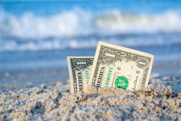 istock Two one dollar bills half buried in sand on sandy seashore close-up. 1396931708