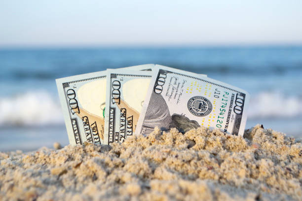 istock Three one hundred dollar bills half buried in sand on sandy seashore close-up 1396931709
