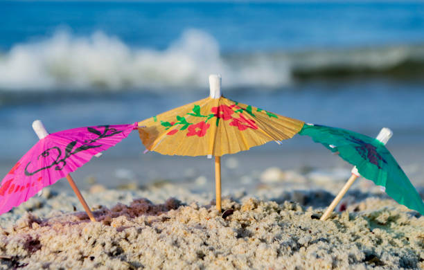 tres pequeñas sombrillas de cóctel de papel se encuentran en la arena en primer plano de la playa de arena - drink umbrella umbrella cocktail pink fotografías e imágenes de stock