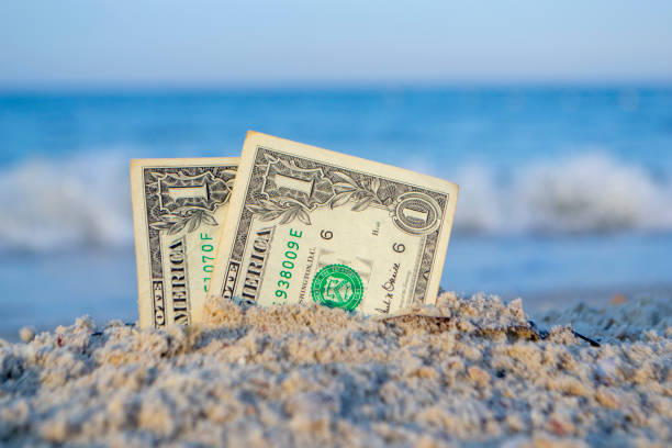 istock Two one dollar bills half buried in sand on sandy seashore close-up. 1396931719