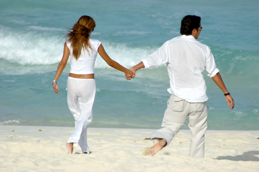Young attractive couple walking along the beach holding hands