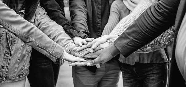 Group of people celebrating together stacking hands outdoor - Black and white editing