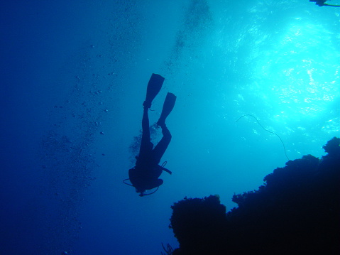 A lone scuba diver swims away from the light towards the deep