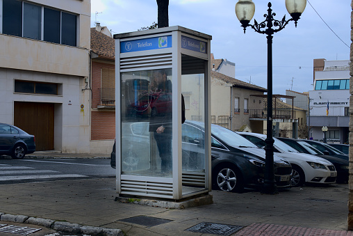 February 2022. Ibi, Alicante, Spain - Misterious man calling at a telephone booth at the street. All phone booths are being removed from all the country. High quality photo