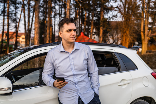 One man young adult businessman using mobile phone while standing in front of his car outdoor in day wearing shirt looking busy real people copy space