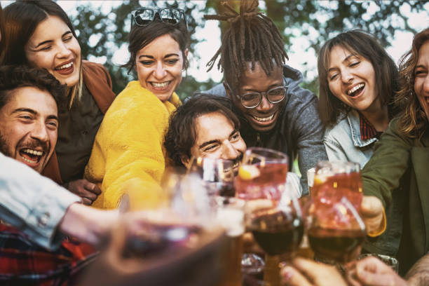 Multiethnic group of excited young people having fun toasting wine and beers together at terrace birthday party - lifestyle concept of multigenerational diverse family stay together - focus center man stock photo