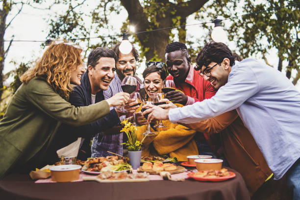 compagnia di amici allegri che si divertono a brindare pic nic nella campagna della fattoria - concetto di stile di vita con amici felici multigenerazionali alza i bicchieri di vino rosso tostati nel giardino sul retro - picnic family barbecue social gathering foto e immagini stock