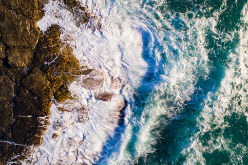 Top down view of ocean waves crashing onto rocky shore