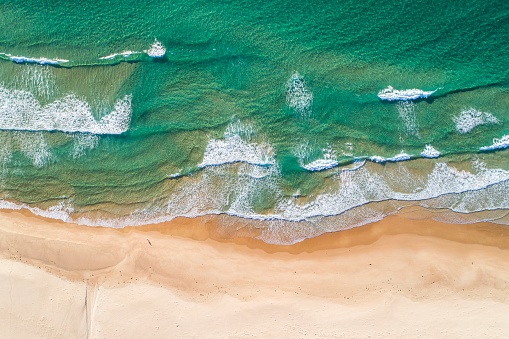 Drone view of pristine clear water ocean waves rolling onto golden sandy beach