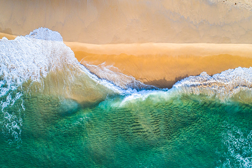 Drone view of emerald ocean waters rolling onto golden sandy shore