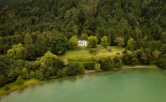Drone view of scenery of cottage located in thick woods on shore of calm pond