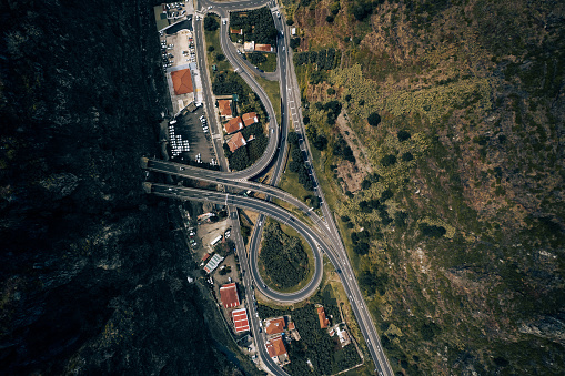 From above drone view of intersection of roadways located near green field and sea