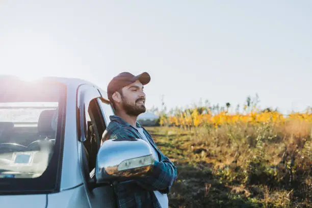 Young latin farmer man leaning on his pickup truck and looking at his plantations. Copy space. Horizontal. High quality photo