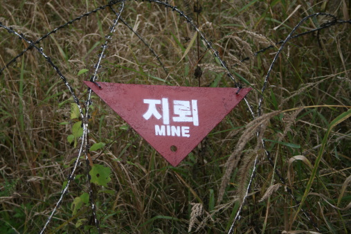 Barbed wire and a mine field sign warn pedestrians where to walk and to avoid.  This is in the DMZ the last seperation and longest wall in the world today.