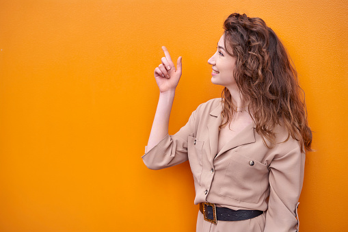 Elegant woman on orange background isolated smiling and pointing finger to the side. High quality photo