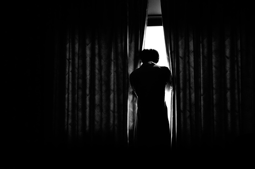 Image of a person looking out through a gap in a dark room curtain ,Monochrome