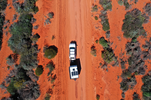 Aerial landscape drone view of 4WD vehicle towing an off road caravan driving on a sand dirt road at Peron Peninsula in Shark Bay, Western Australia.