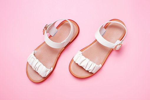 Female beige sandals on a pink background close up top view.