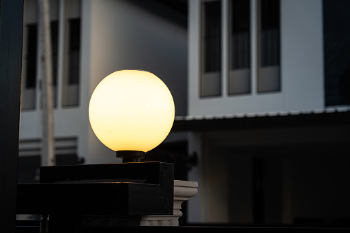 A classic style street lighting lamp is glowing in orange warm light shade in evening night time with background of building structure. Photo contained noise due to dark condition. Selective focus.