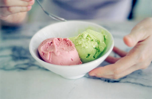 ice creams in a bowl a strawberry italian style gelato and a lime sorbet in a white bowl with hands and spoon on the sides appitite stock pictures, royalty-free photos & images