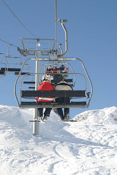 A chair lift takes a pair of skiers to the top of a mountain on a beautiful alpine day