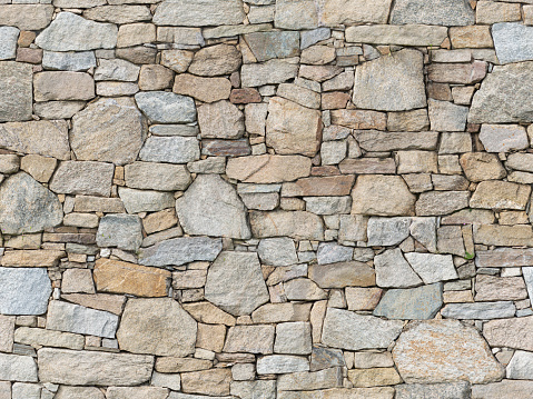 A fragment of a city wall of hewn stone on cement mortar. Stones of different sizes and colors, but in the same style.