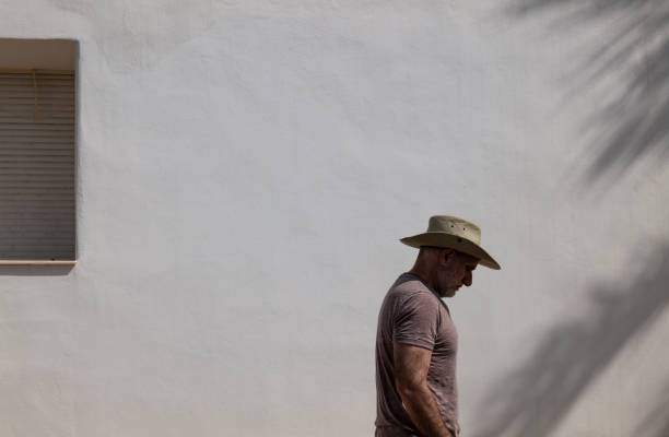 vista laterale dell'uomo adulto in cappello da cowboy contro il muro bianco in una giornata di sole - the western wall foto e immagini stock