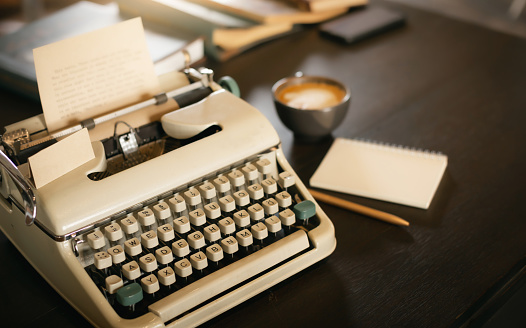 Old typewriter on wooden table with note book and coffee drink, desk office of writer, retro style and darktone