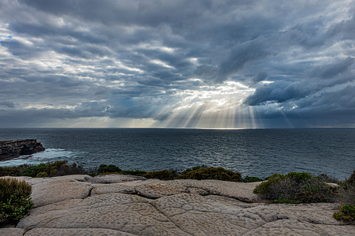 Sunbeams pour out of clouds over a beautiful calm ocean.