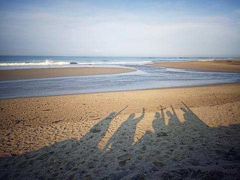 Light and shadows of people sitting on beach with raise hands. Family, friendship togetherness concept. Inspirational backgrounds with copy space.