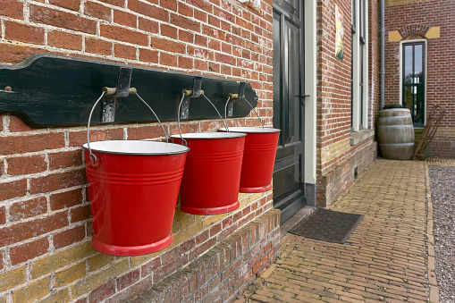 Three red metal fire buckets hanging in a row on a brick wall at an old train station.