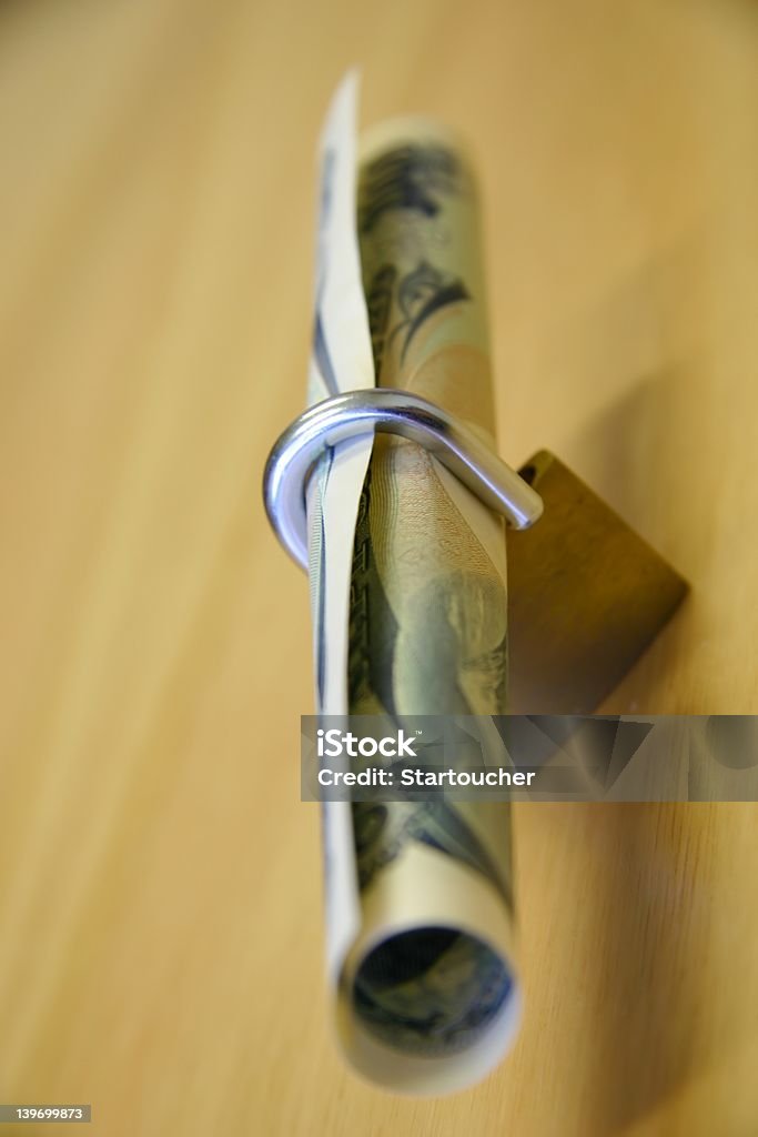 Bank note and open padlock Bank note rolled up inside an open padlock on a wooden desk Arrival Stock Photo