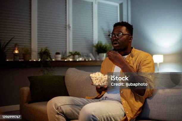 Serious Young Guy Taking Some Popcorn From A Bowl While Watching Horor Movie Stock Photo - Download Image Now