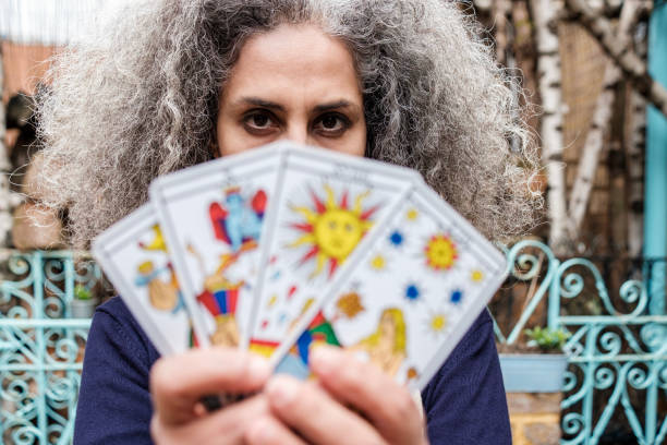 Psychic mature woman reader showing us out of focus tarot cards. Her hair is curly and grey.