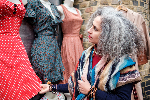 Mature woman watching outfits in a street market in London. She is wearing a colorful scarf.