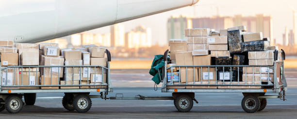 vista dettagliata ravvicinata del carrello del carrello di carico pieno di pacchi commerciali contro l'aereo da carico turboelica. spedizione e logistica della posta aerea. operazioni di import export. servizio di voli charter commerciali - baggage wagon foto e immagini stock